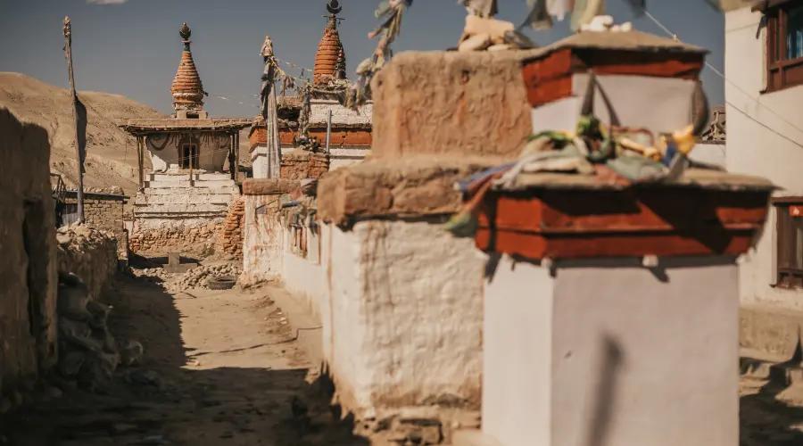 Traditional Buddhist chortens and stupas decorated with prayer flags along a mountain trail in a remote Himalayan village.